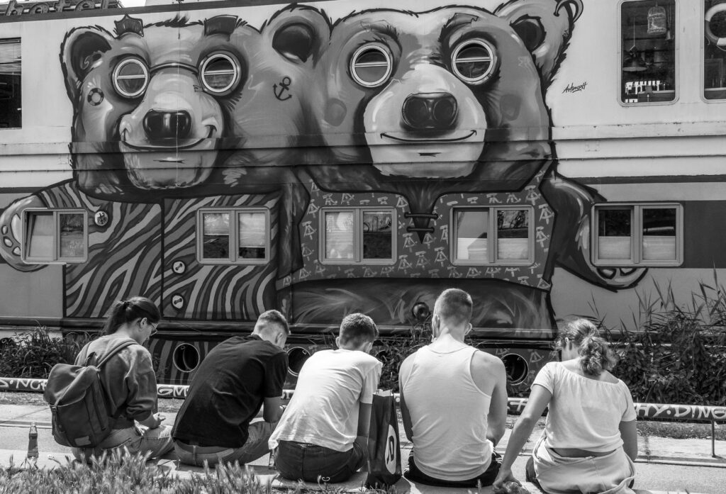 eine Gruppe von jungen Menschen sitzt vor einem Bären Graffiti auf einem Zug. Das Bild ist schwarz/weiss